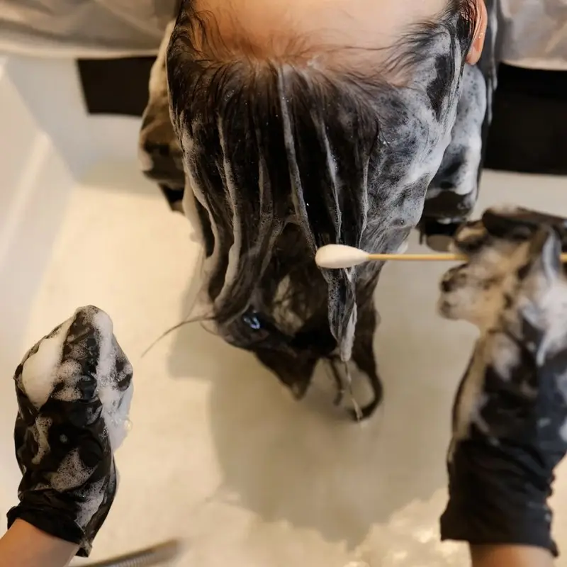 Gloved hands lathering a guest's scalp over the basin during the staged cleanse of a Korean head spa, the second of the seven stages in a 60-minute head spa treatment